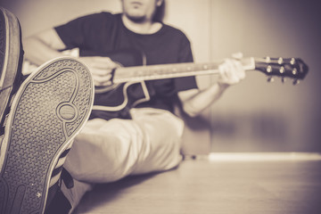 Junger Mann spielt Gitarre, sitzend am Boden, schwarz weiß