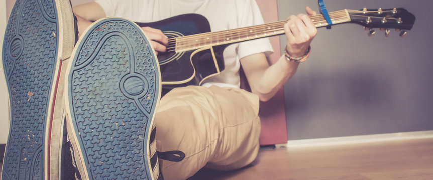 Junger Mann spielt Gitarre, sitzend am Boden