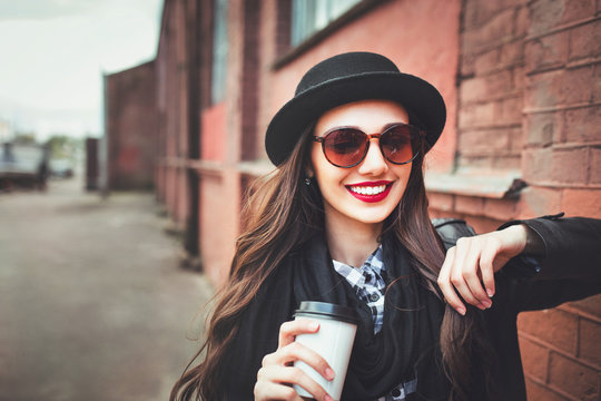 Fashion woman wearing sunglasses and a hat with a drink outdoors. Young woman wearing sunglasses on the street and holding a cup of coffee