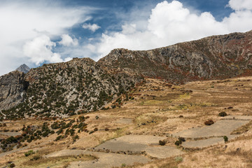 Mountain pastures with yak grazin under dramatic sky.
