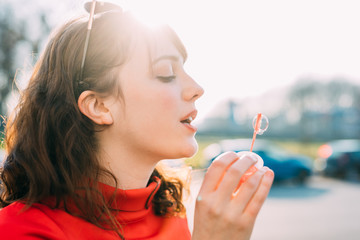 Portrait of young beautiful red dressed vintage hipster woman playing with bubble soap blowing - childhood, having fun, happiness concept