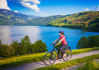 Naklejka premium woman with e-bike cycling beside a beautiful lake-lake and bike