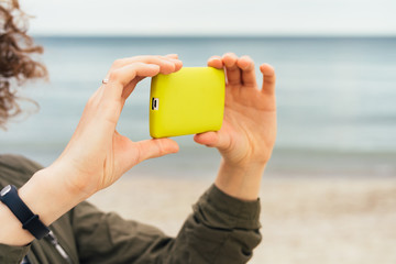 Woman holding a yellow mobile phone with two hands on the beach