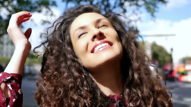 Portrait of happy young woman with beautiful curly hair smiling in the city, slow motion