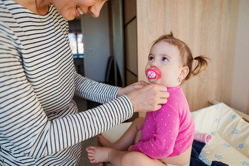 Mother dressing her daughter in the morning in bedroom