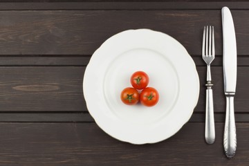 Very strict diet. Dietary vegetable diet. Tomatoes on a plate. Slimming diet. White plate with tomato on dark table.
