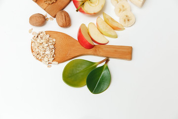 There are Banana,Aple,Orange with Walnuts in the Wooden Plate and Rolled Oats,Wooden Spoon,Trivet,with Green Leaves,Healthy Fresh Organic Food on the White Background