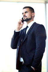 Fototapeta premium Young businessman standing in office lobby, using smartphone