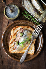Rustic sandwich with canned sardines, capers and fresh thyme on dark wooden background. Overhead view