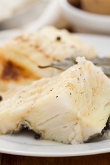 boiled cod fish with black pepper on white plate and potato in white bowl