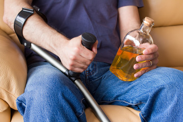 man with crutches holding bottle of alcohol