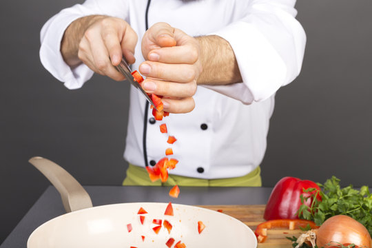 Chef hands putting chopped red pepper in a pan