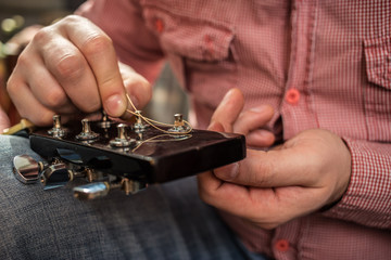 male inserts new guitar strings to the acoustic guitar