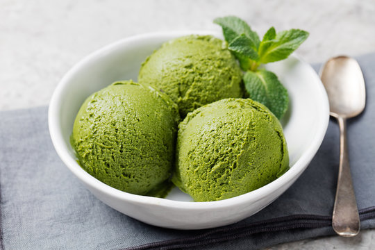 Green tea matcha ice cream scoop in white bowl on a grey stone background
