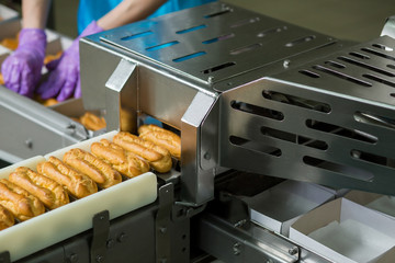 Eclair shells and white boxes. Eclairs on conveyor beside worker. Complex machine at confectionery plant. Production of baked food.
