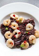 Black rice noodles with shrimps, prawns, white table, gray background. 