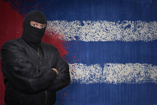 dangerous man in a mask standing near a wall with painted national flag of cuba