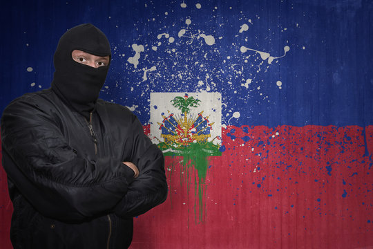 dangerous man in a mask standing near a wall with painted national flag of haiti
