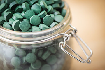 Spirulina supplement pills into airtight jar. Antioxidant alga nutrition.