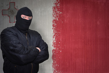 dangerous man in a mask standing near a wall with painted national flag of malta