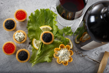 Tartlets filled with red and black caviar and seaweed salad with a wine glass and bottle against...