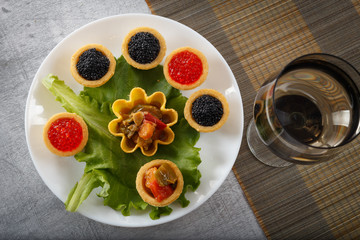 Tartlets filled with red and black caviar and cheese and dill salad on white plate against white wooden background