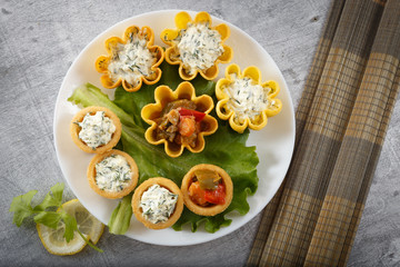 Tartlets filled with vegetables and cheese and dill salad on white plate and leaf against rustic wooden background