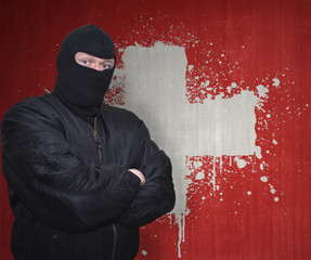 dangerous man in a mask standing near a wall with painted national flag of switzerland