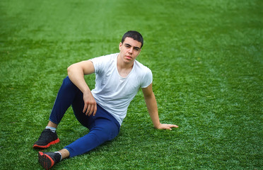 Fototapeta na wymiar Young smiling sportsman sitting on grass