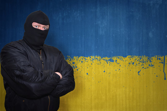 dangerous man in a mask standing near a wall with painted national flag of ukraine