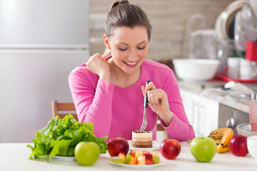 Young woman is eating a cake instead of healthy fresh fruit and vegetable on the table