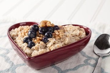 Heart shaped bowl with oatmeal, blueberries, and walnuts with spoon on a blue and white place mat