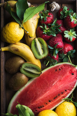 Various colorful tropical fruit selection in wooden tray over dark background