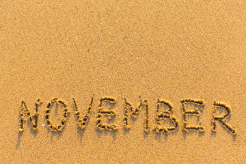 November - word inscription on the gold sand sea beach.
