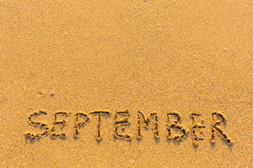 September - word inscription on the gold sand sea beach.