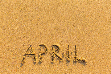 April - word inscription on the gold sand sea beach.