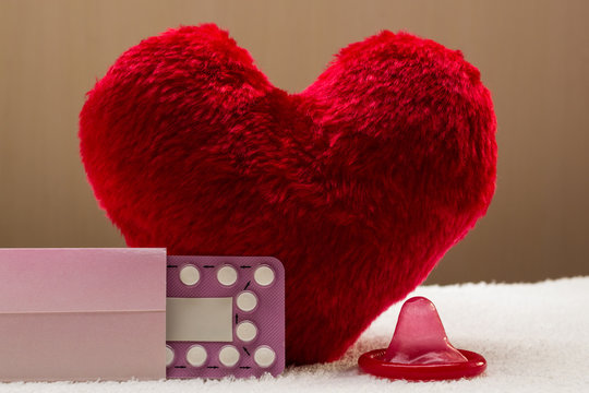 Oral contraceptive pills condom on red heart