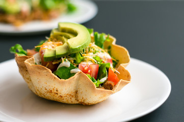 Taco salad in tortilla bowl is a fun and colorful way to eat mexican food. Made with fresh ingredients such as avocado, tomatoes, green salad, cheese and delicious sour cream vinaigrette.
