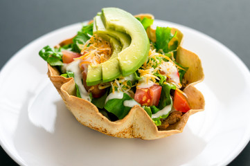 Taco salad in tortilla bowl is a fun and colorful way to eat mexican food. Made with fresh ingredients such as avocado, tomatoes, green salad, cheese and delicious sour cream vinaigrette.