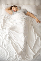 Obraz na płótnie Canvas Young man sleeping alone in white big bed