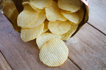 Opened pack with potato chips over wooden table