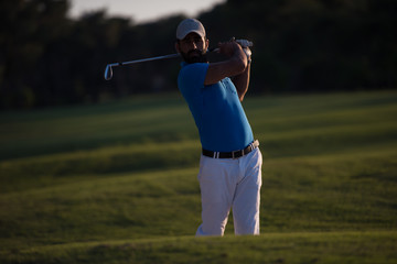 golfer hitting a sand bunker shot on sunset