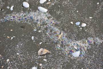 Colourful bubbles of detergent foam on beach sand.