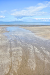Distant volcano island view from flat sandy beach at low tide.