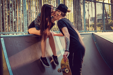 Sexual brunette kissing tattooed skater in skate park. - obrazy, fototapety, plakaty