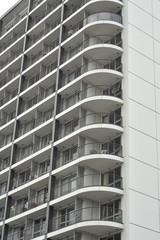 Modern tall concrete apartment building having one wall covered with balconies.