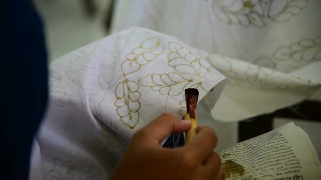 Using pen-like tool used to apply liquid hot wax n the batik-making process.