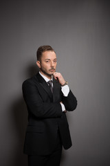 Portrait of businessman looking at camera without any emotions. Handsome man standing and touching his cheek in studio.