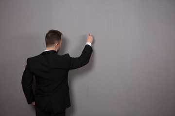 Back view of businessman writing something on wall in studio. Young man in black suit explaining some diagrams or projects.