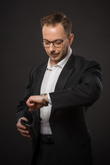 Portrait of businessman in black suit and glasses checking time. Handsome young man looking at his watch not to be late for business meeting.